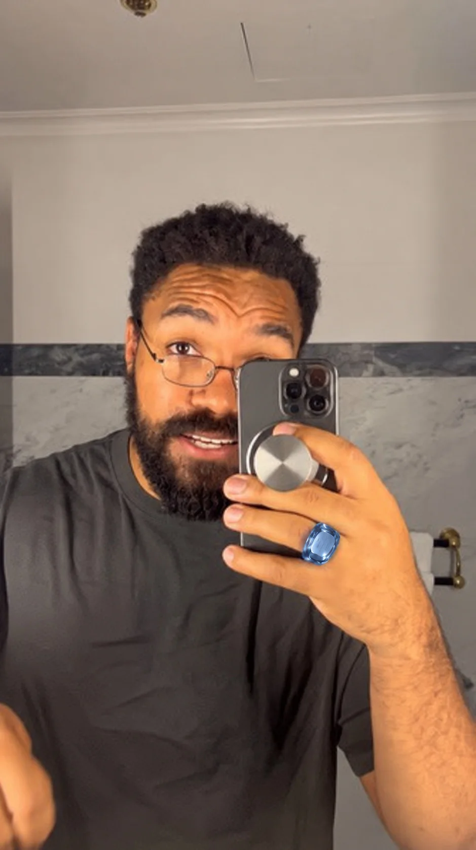 A man takes a mirror photograph, his phone raised in one hand. On that hand he wears the House Armure ring in sapphire blue.